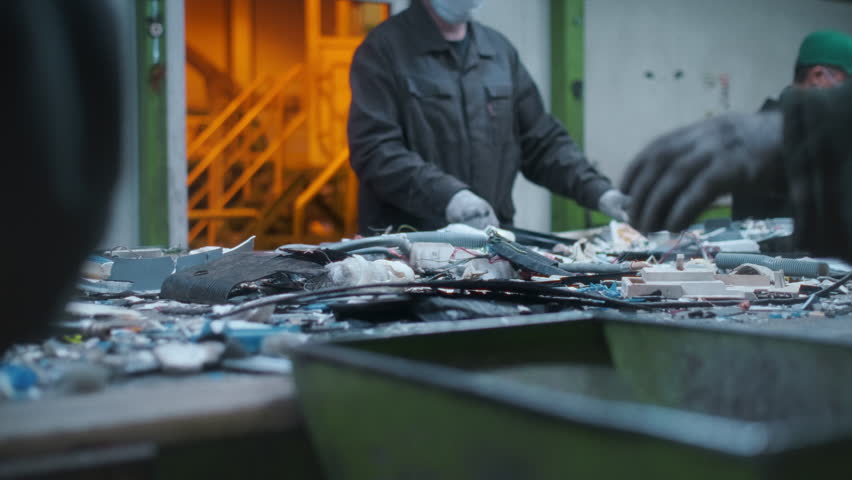 Men workers of garbage processing plant sort garbage. Male workers sort and recycle scrap metal. Plastic, polymer household waste is transported on conveyor belt in factory. Ecology of planet. Man
