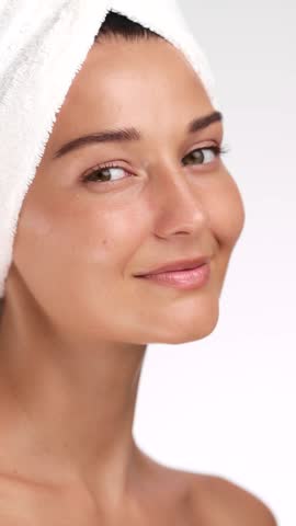 Caucasian woman with glowing skin and a towel on her head gently touches her face, representing skincare, wellness, and beauty concepts in a high quality spa-like setting.