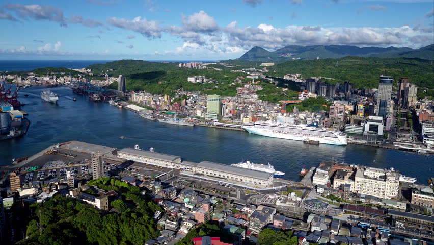 Aerial hyperlapse footage of a cruise ship assisted by pilot boats to navigate the blue water and berth in Keelung Harbor, which is a vibrant seaport city and a tourist destination in northern Taiwan