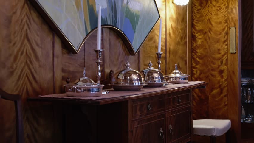 Silver serving dishes and tall candlesticks on a wood buffet in an ornate dining room