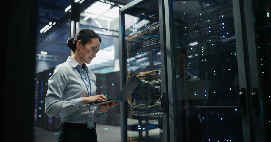 Data Center Female IT Specialist Using Laptop in Server Room. Artificial Intelligence Computing Facility with Asian Maintenance Administrator Working on Computer. Information Technology Professional