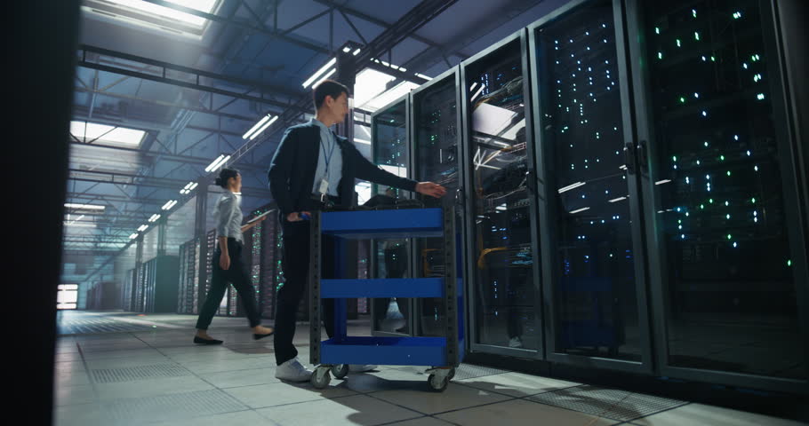 Asian Male Software Developer Walking Up to a Server with a Pushcart in Order to Run Diagnostics on a Laptop Computer. Technical Manager Checking Settings for AI Infrastructure in a Data Center