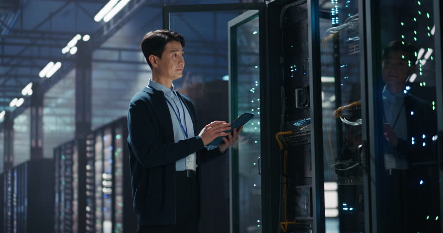 Data Center Administrator Using Tablet Computer. Asian Maintenance Specialist Working on Cyber Security and Network Protection in AI Computing Facility. Engineer Checking Server Farm Analytics