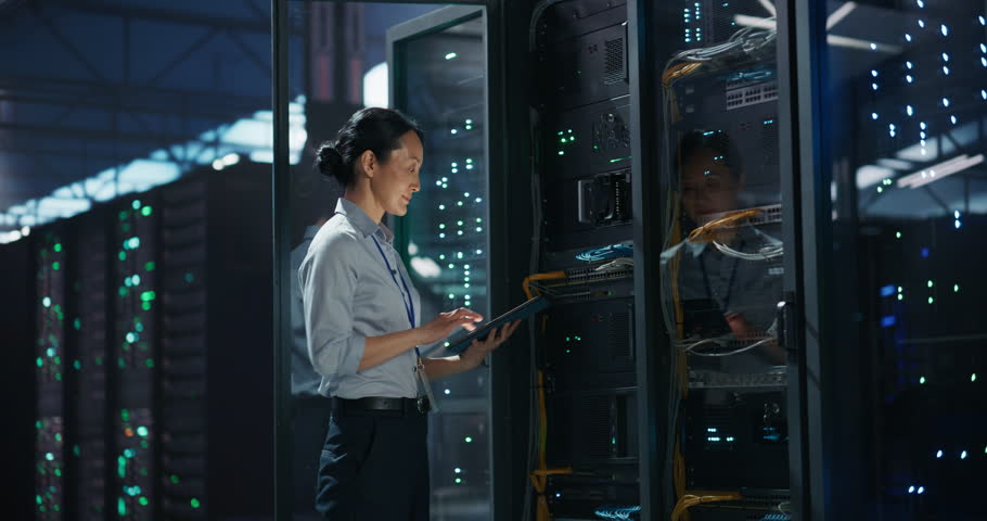 Data Center Female IT Specialist Using Tablet in Server Room. Artificial Intelligence Computing Facility with Asian Maintenance Administrator Working on Computer. Information Technology Professional