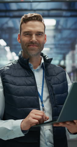 Vertical Screen: Data Center Engineer Using a Laptop Computer. Adult Man Looking at Camera and Smiling. Information Technology Specialist Standing in a Facility with Operational Server Racks