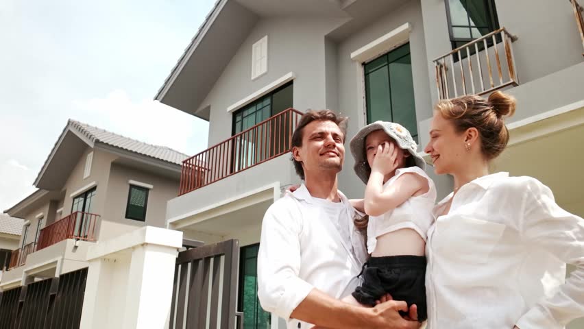 Happy family standing outside their new home, pointing with excitement. Ideal for real estate, family living, and housing market ads promoting new beginnings and home ownership success.