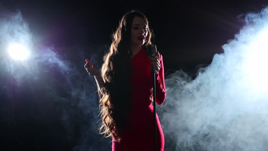 Singer in a dress with a microphone in her hands sings in the rays of spotlights and a smoky stage