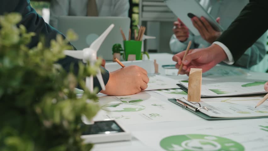 A group of professionals engages in a collaborative meeting focused on sustainable development, utilizing renewable energy concepts and eco-friendly planning documents. SACTR