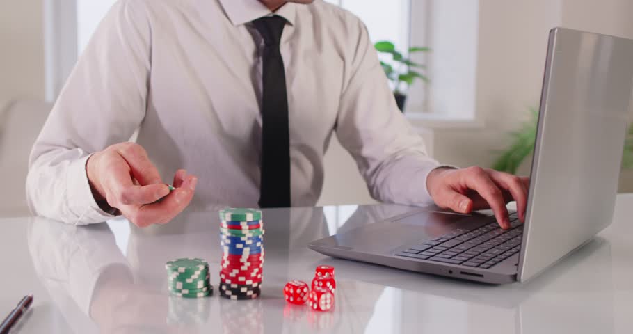 Excited overjoyed man at computer desk holding online casino poker chips, jetons, winner feeling euphoric with bet gambling victory, looks at screen celebrates fantastic news, received best prize