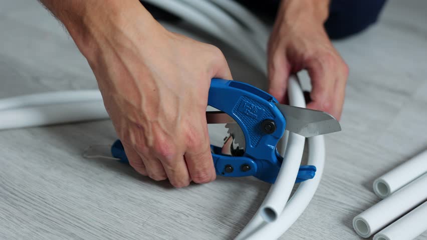 Plumber cuts a piece from a plastic pipe using a pipe cutter with a ratchet mechanism in close-up