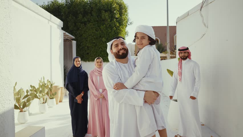 Muslim family, father, mother, son and daughter, wearing traditional clothes, are posing together in their house's courtyard, smiling and looking at each other - Powered by Shutterstock - Get 15% off with code: PIKWIZARD15