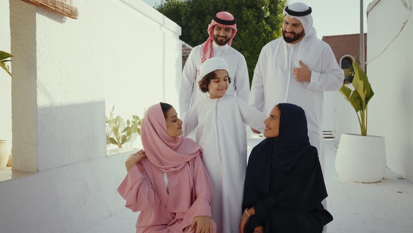Muslim family, father, mother, son and daughter, wearing traditional clothes, are posing together in their house's courtyard, smiling and looking at each other