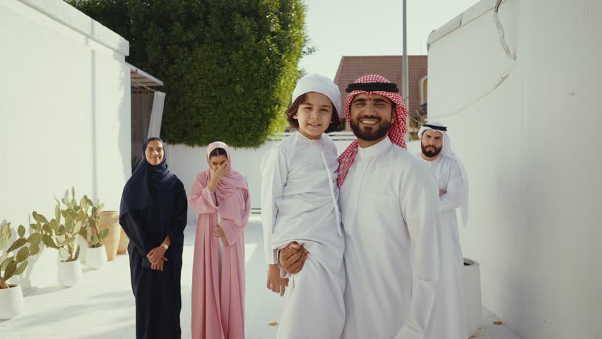 Muslim family, father, mother, son and daughter, wearing traditional clothes, are posing together in their house's courtyard, smiling and looking at each other