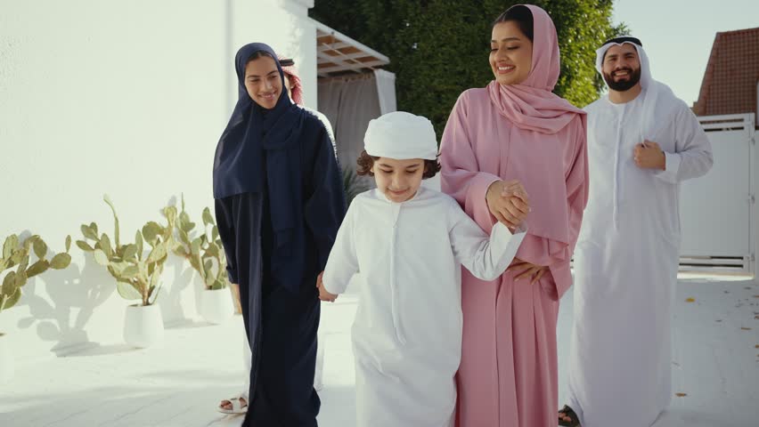 Muslim family, father, mother, son and daughter, wearing traditional clothes, are posing together in their house's courtyard, smiling and looking at each other