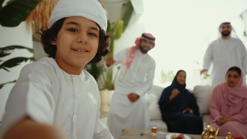 Emirati family members wearing traditional kandura and abaya posing together on couch, sharing warm smile during festive family gathering in decorated home interior