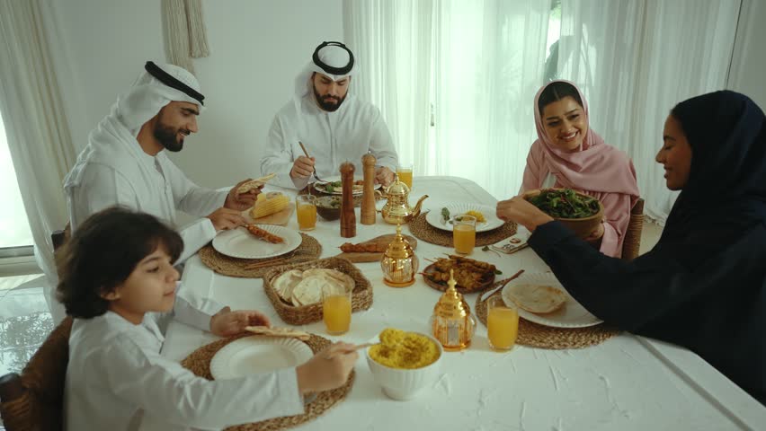 Emirati family sharing a meal together during the holy month of ramadan, passing dishes and engaging in conversation around a beautifully set table