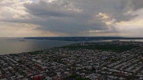 Aerial view of Bensonhurst, Brooklyn in the late afternoon just before a rainstorm. Sunlight breaks through dramatic clouds, casting warm highlights over residential rooftops and tree-lined streets. T - Powered by Shutterstock - Get 15% off with code: PIKWIZARD15