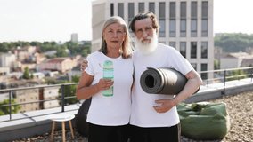 Senior man and woman outdoors on rooftop holding yoga mat and water bottle smiling showing active lifestyle and happiness. Captures healthy living, exercise, and connection against urban cityscape - Powered by Shutterstock - Get 15% off with code: PIKWIZARD15