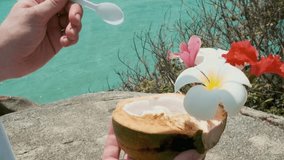Fresh coconut ice cream with tropical flowers held by person hands and preparing to eat summer tropical dessert using spoon with seaside background, Samui island, Thailand - Powered by Shutterstock - Get 15% off with code: PIKWIZARD15
