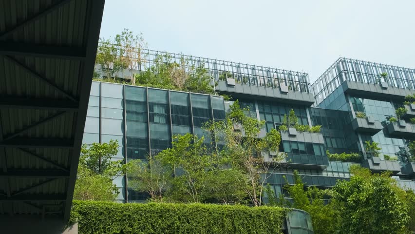 Sustainable glass office building facade with green plants growth on the wall. Vertical garden in Bangkok city, Thailand. Eco friendly urban environment. Modern biophilic and ecological architecture