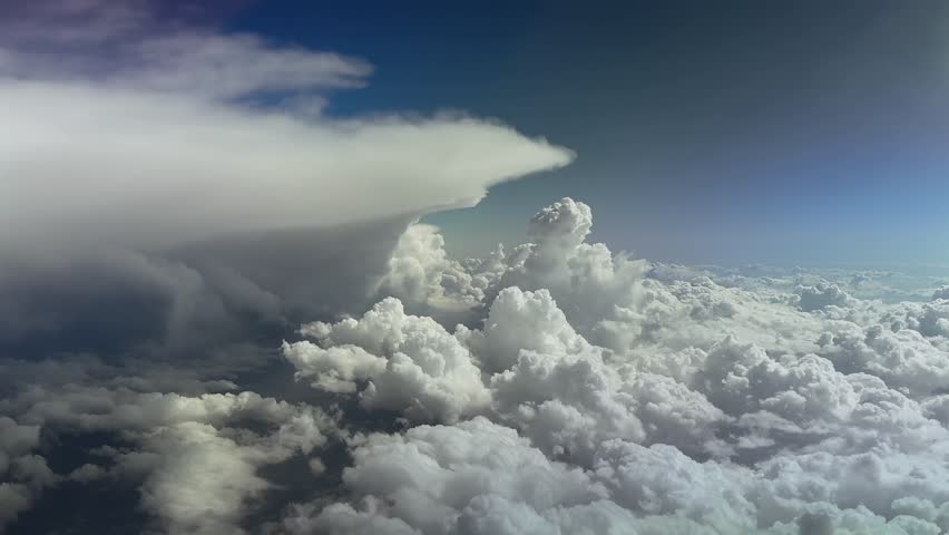 an immersive aerial pilot’s view of massive storm clouds under an intense color blue sky.