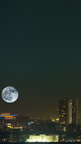 Huge full moon rising over the Abu Dhabi city skyline in the United Arab Emirates - zoomed in vertical time lapse