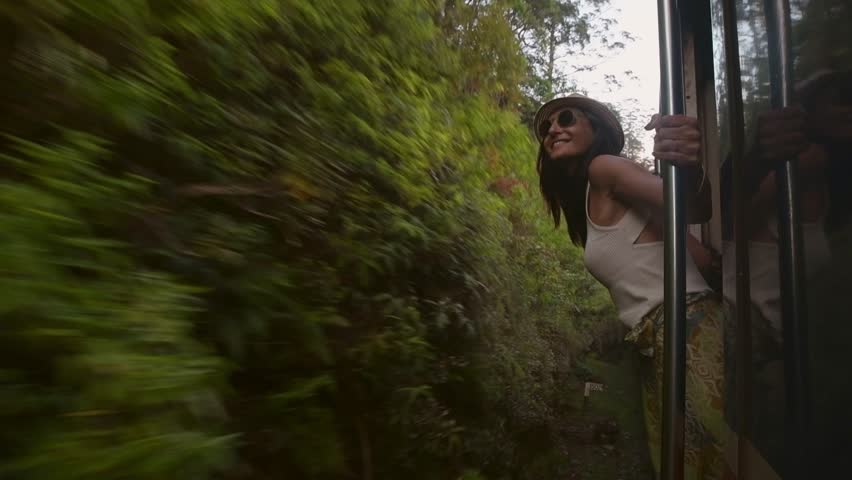Happy passenger woman tourist stand by doorstep enjoy popular train ride journey Kandy to Ella and admire Sri lanka lush jungle landscapes. Embrace freedom, curiosity, wonder and serenity concept