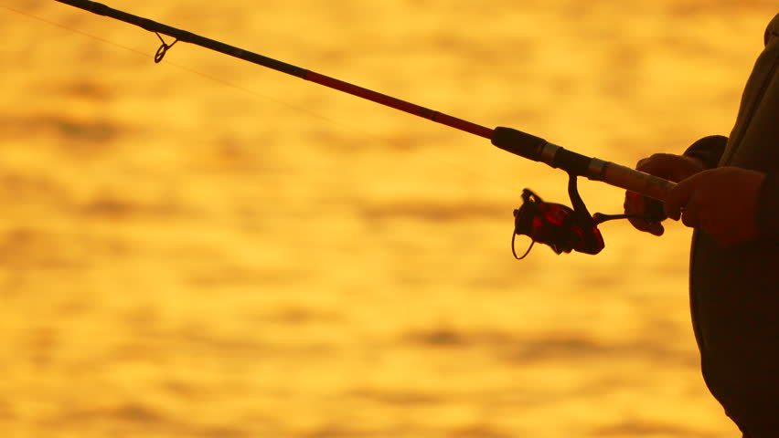Fishing Sunset Silhouette: Man Reels in Catch, Golden Hour Lake Fishing