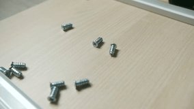 Man wearing protective gloves carefully takes small metal screws on wooden surface, preparing components for furniture assembly process. Worker picking up screws furniture assembly on wooden surface - Powered by Shutterstock - Get 15% off with code: PIKWIZARD15