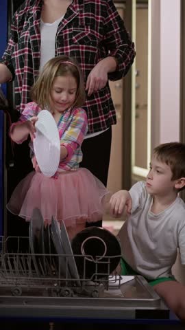 Mother and children put dirty dishes in the dishwasher. Son and daughter help parents with household chores.