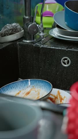 Woman hands wash dirty dishes in the sink with running water after a family meal showing daily household routine and cleanliness in the kitchen.