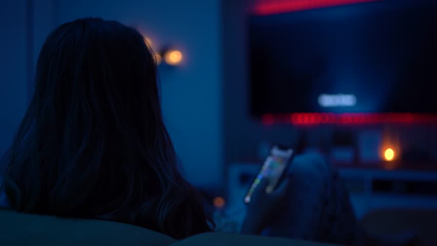 Home Alone Relaxation Concept: Woman Watching Television in the Evening with Snacks and a Cozy Mood