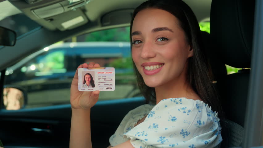 Happy smiling Caucasian joyful girl woman female driver sitting inside new car showing driving license at camera successfully passed test exam drive courses. Transportation test drive automobile rent