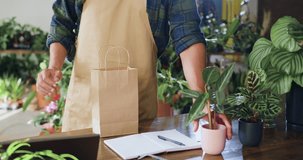 Shopping in flower store. Florist manager working in floral greenhouse. Close up hands man florist worker packs in paper bag and selling house plant in flower shop. People and business concept. - Powered by Shutterstock - Get 15% off with code: PIKWIZARD15
