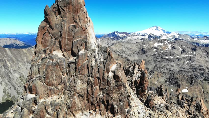 Ascending drone view of sharp granite peak Torre Principal, revealing Cerro Tronador in distance and clear sky, Frey, Bariloche, Argentina.