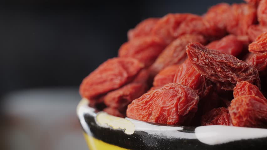 Dried goji berries in bowl and spoon on wooden table, closeup. Space for text