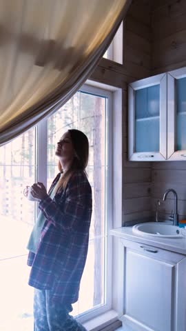 Young woman enjoying her favorite music, dancing in the kitchen in the morning and drinking coffee.