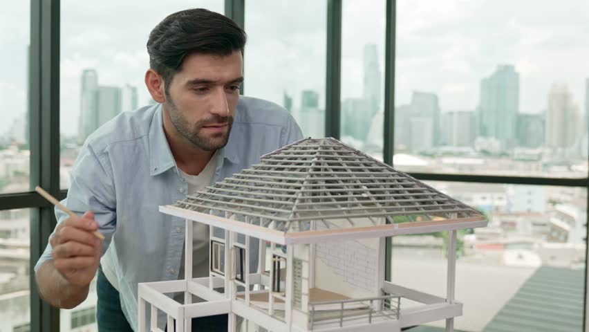 Professional architect engineer using pencil measuring model roof length at modern office with skyscraper, cityscape view. Skilled project manager or businessman check house construction. Tracery