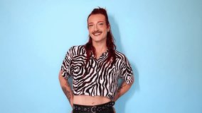 Confident non-binary model with red hair and mustache posing on blue background, expressing gender identity while smiling and changing poses - Powered by Shutterstock - Get 15% off with code: PIKWIZARD15