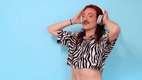 Happy non-binary person with long red hair, mustache and zebra-striped shirt dancing and listening to music with headphones on a blue background - Powered by Shutterstock - Get 15% off with code: PIKWIZARD15