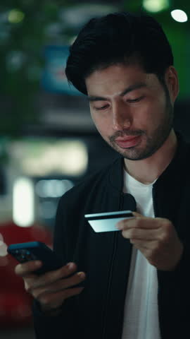 Young dark haired male holding smartphone and credit card while processing cashless payment online, Concentrated person copying data in application while completing shopping through device.