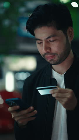 Young dark haired male holding smartphone and credit card while processing cashless payment online, Concentrated person copying data in application while completing shopping through device.