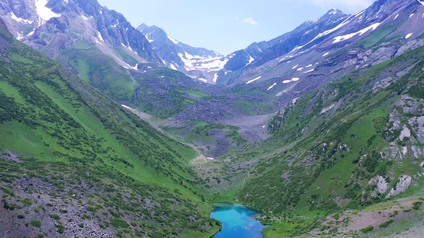 Aerial view of a mountain valley with a blue lake, green slopes, and snow-capped peaks in Canada.