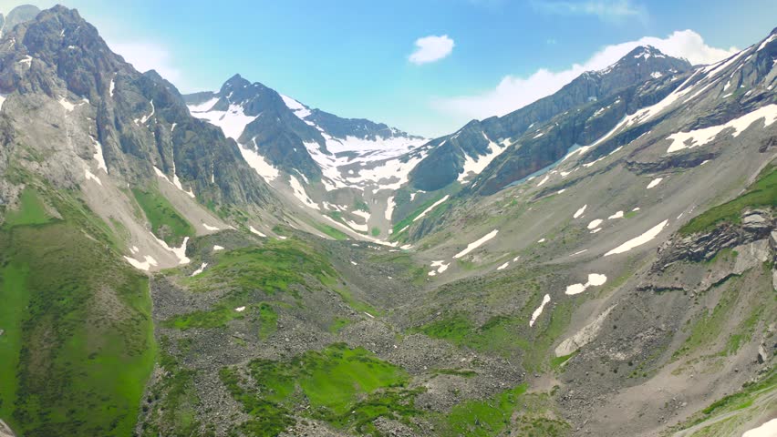 Aerial view looking down into a mountain valley showing snow patches and green slopes. Location Canada.