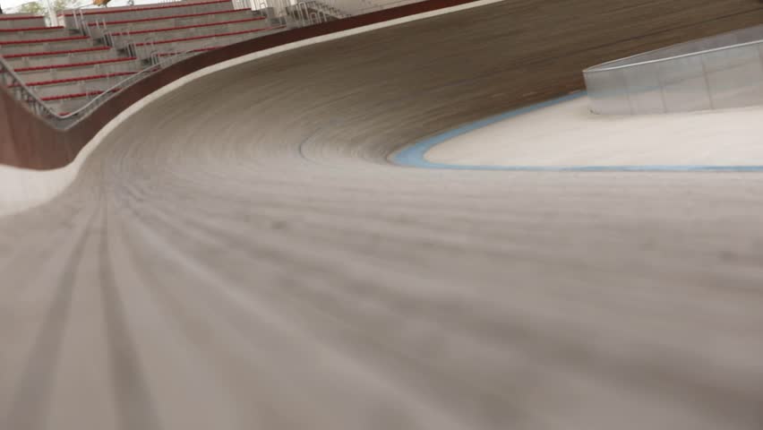 Group of cyclists race at high speed on a banked wooden velodrome track. Low angle view captures the dynamic action during a competition or training session.