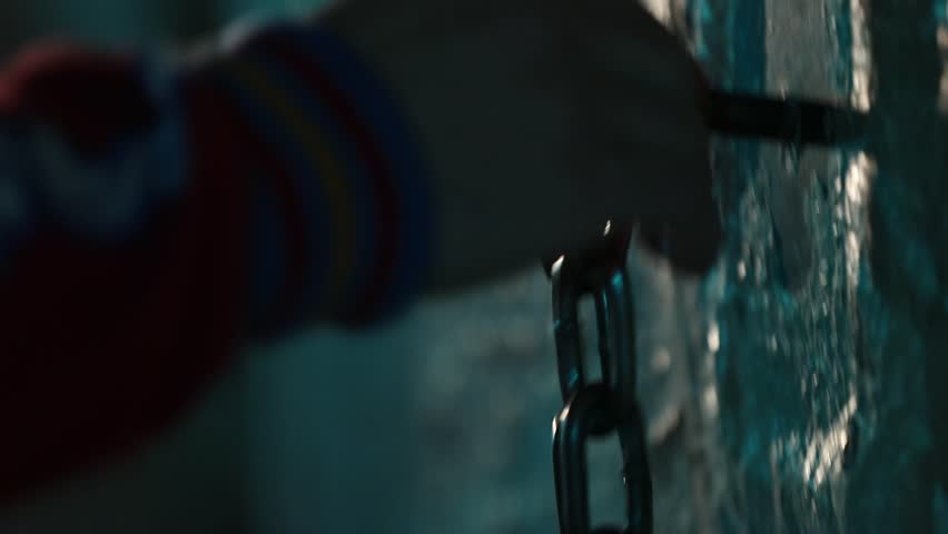 Two dark hanging straps slowly twist and turn. A striking blue light dramatically defines their edges against a mysterious, blurred background. Close-up detail.