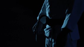 Close-up: Martial artist in meticulously ties their black belt in slow motion. Dark, moody atmosphere with cool blue lighting emphasizes focus and pre-fight ritual. - Powered by Shutterstock - Get 15% off with code: PIKWIZARD15