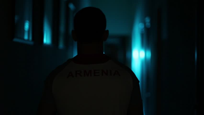 man  walking down dark, blue-lit corridor. He slings a sports bag over his shoulder. Mysterious, atmospheric, purposeful journey.