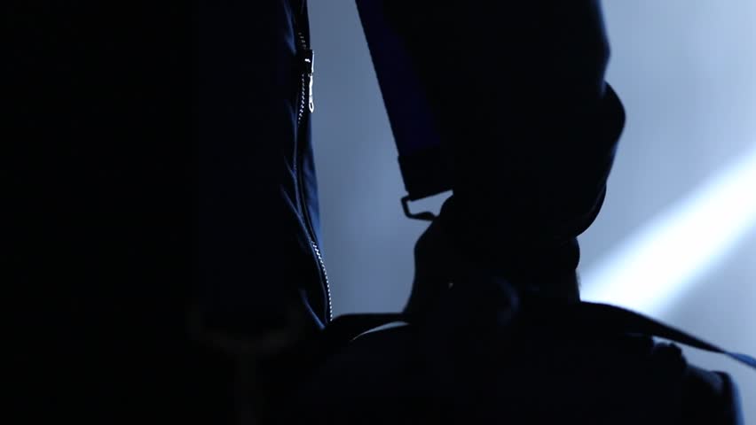 man  walking down dark, blue-lit corridor. He slings a sports bag over his shoulder. Mysterious, atmospheric, purposeful journey.
