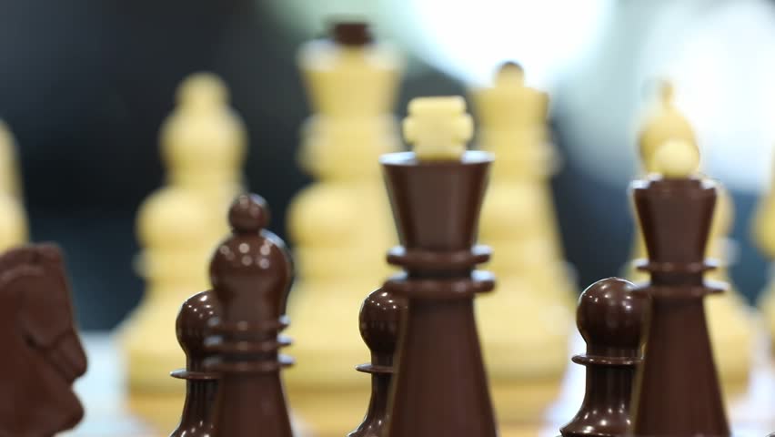 Close-up footage of two players making opening moves in a chess game. Hands strategically position white and black pieces on the wooden chessboard, initiating the intellectual battle.